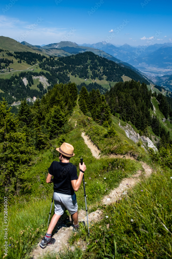 Hiker with poles on a mountain ridge trail with mountain views into the distance