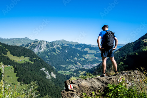 Hiker standing on a mountain admiring the view over the valley with a village in the valley