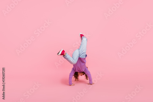 Full length photo of playful fooling little child dressed purple pullover walking arms upside down isolated pink color background