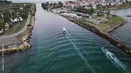 Two fishing boats sailing  through a sea canal with calm water and birds flying above them at Potidea Halkidiki Greece during sunset summer season, drone clip 4k 60 FPS photo