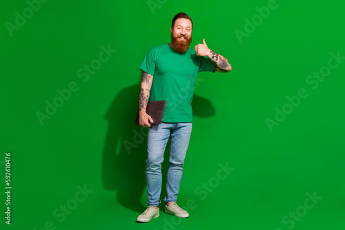 Full length photo of confident positive man wear t-shirt showing thumb up holding modern gadget isolated green color background