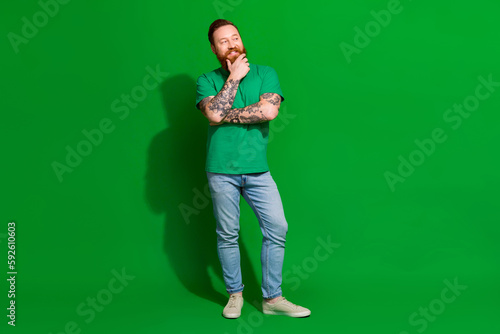 Full length photo of cheerful dreamy guy dressed t-shirt smiling arm chin looking empty space isolated green color background