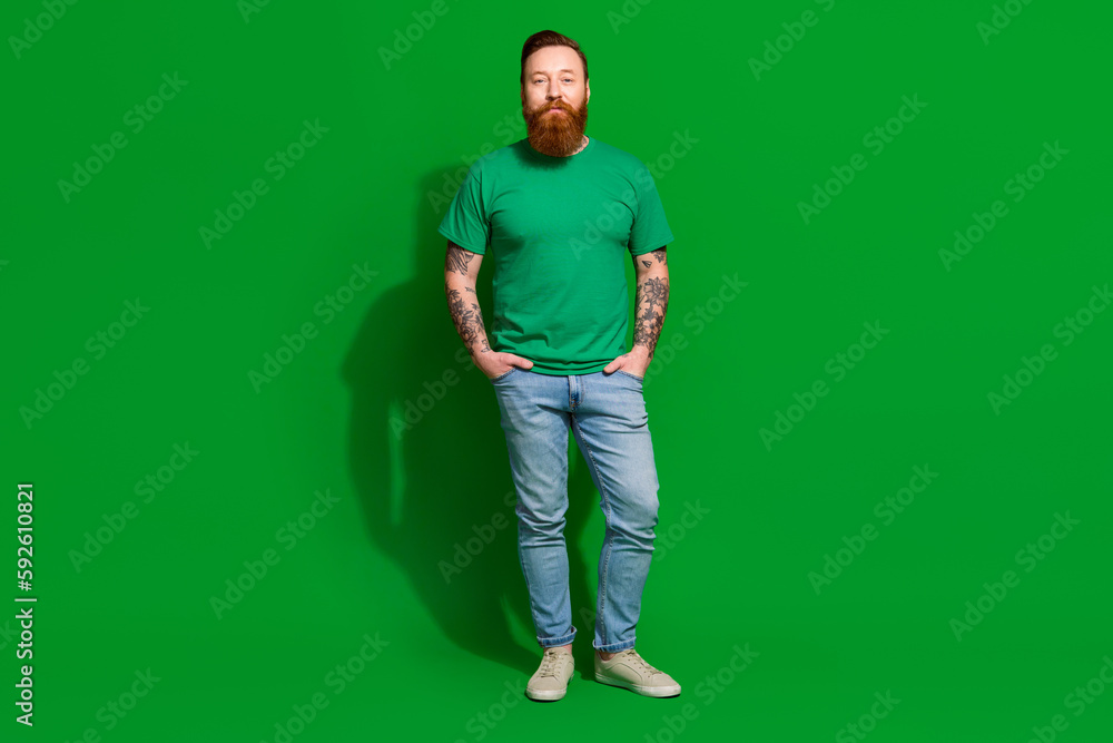 Full length photo of serious confident man wear t-shirt arm hands pockets walking isolated green color background Full length photo of serious confident man wear t-shirt arm hands pockets walking isolated green color background
