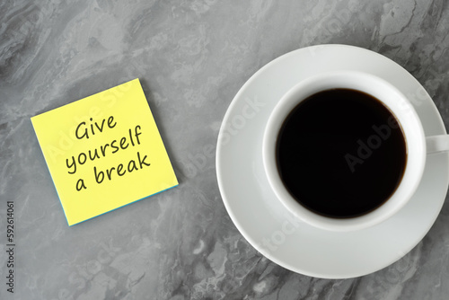 Cup of coffee and adhesive note with text Give yourself a break