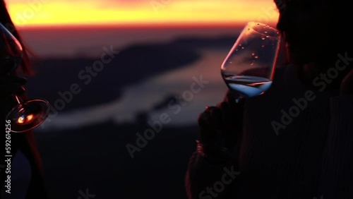 woman wine drinking at sunset outdoors with mountains and sea view. Two friends wine drinking with beautiful view at sunset silhouette. Wine tasting outdoors. 