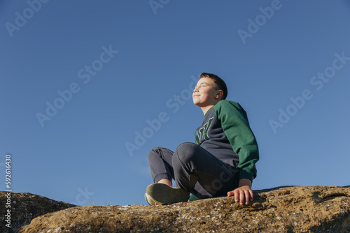  boy sitting on a rock against the blue sky
