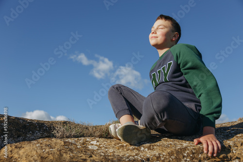 dreaming boy sitting on a rock against the blue sky