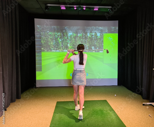 Professional female golfer holding club playing golf indoors on golf simulator