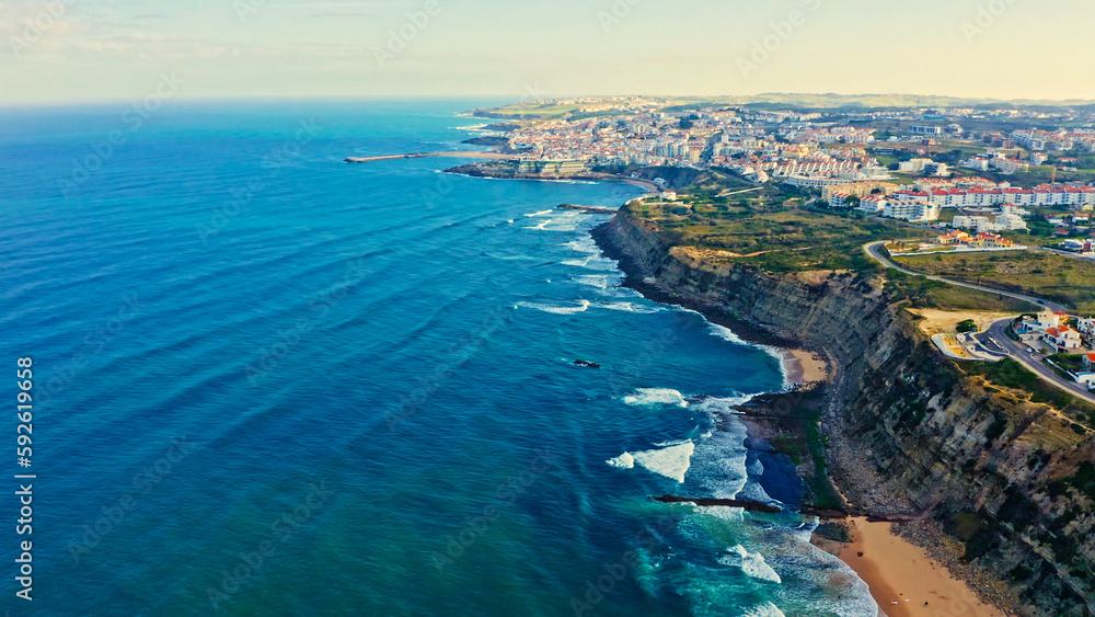 Panorama of the city from a drone with a  rocky ocean coastline during sunrise. Scenic summer  landscape  from drone. Drone view of a beautiful tourist town located on the shore of the Atlantic Ocean.