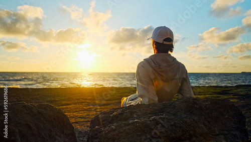 Man on a beach is looking distance during beautiful summer sunset. Human looks to the sun over horizon in the morning while sunrise. Happy person contemplates the beauty of nature. Freedom concept.