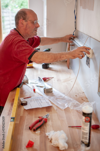 Kitchen Fitters: Electrical Installation.An electrician installing a strip light onto new kitchen build splashback. From a series of related images. photo