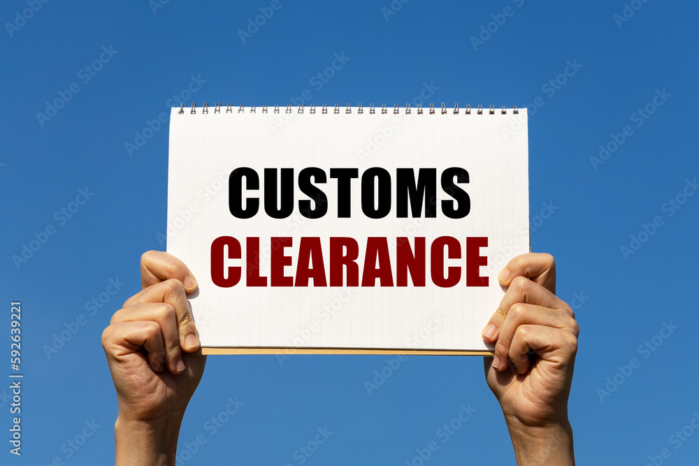 Customs clearance text on notebook paper held by 2 hands with isolated blue sky background. This message can be used as business concept about customs clearance. Customs clearance text on notebook paper held by 2 hands with isolated blue sky background. This message can be used as business concept about customs clearance.