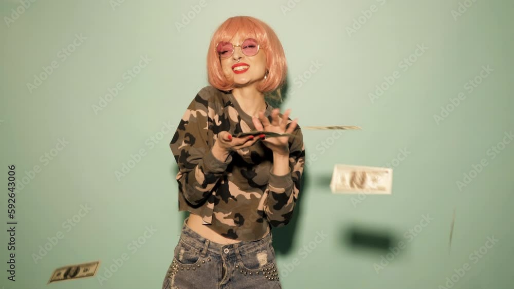 Young beautiful hipster bad girl in trendy summer clothes and earring in her nose. Sexy carefree woman in studio in pink wig near wall. Model throwing out falling money dollars banknotes. Money rain Young beautiful hipster bad girl in trendy summer clothes and earring in her nose. Sexy carefree woman in studio in pink wig near wall. Model throwing out falling money dollars banknotes. Money rain