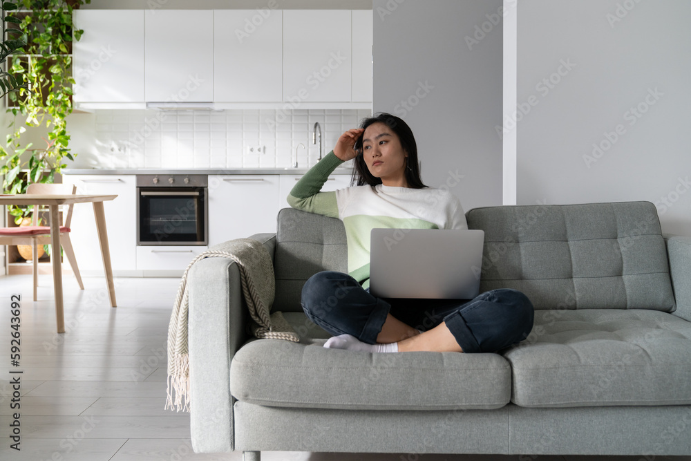Foto de Thoughtful young Asian woman freelancer tired sits on sofa with