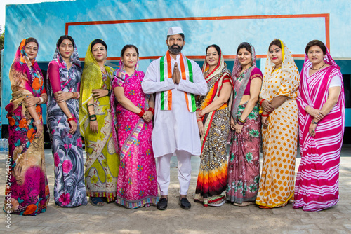 Indian man politician standing doing namaste with group of traditional women. Concept of election and vote.