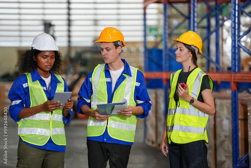 Multiethnic industrial workers checking their logistic lists while working with transportation of goods in warehouse Multiethnic industrial workers checking their logistic lists while working with transportation of goods in warehouse