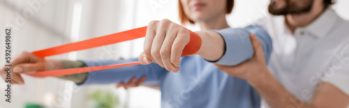Bilde på lerret cropped view of physiotherapist supporting arms of woman training with resistance band in rehab center, banner