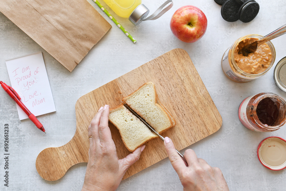 Mom making PB&J sandwich while packing lunch for child. Flat lay food ...