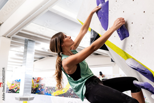 Woman climbing bouldering wall with grips photo