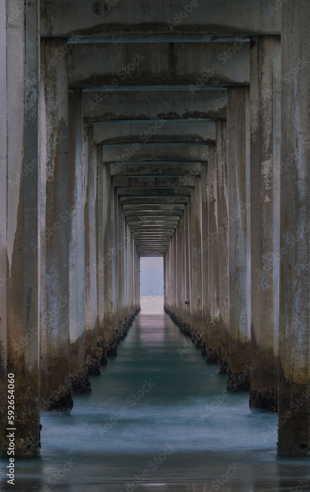 Stairway to Heaven: The pillars of the pier steam out towards the ocean like a tunnel as the waves gently lap the shore of a beach in La Jolla, California