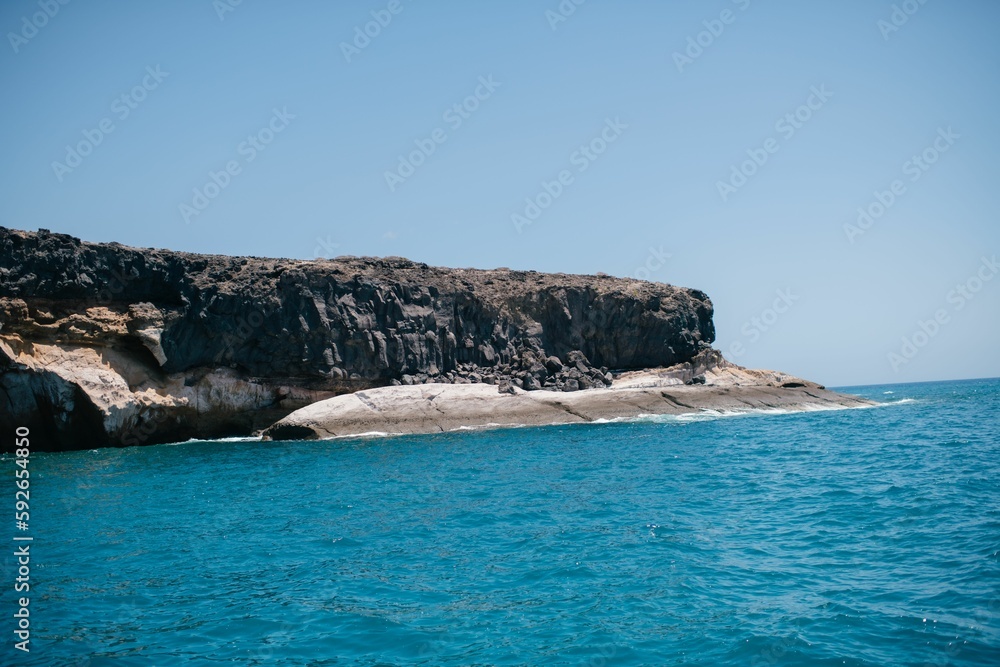 Obraz premium Seascape of a calm blue water with rocky cliff on a sunny day