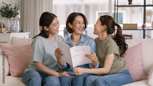 Buy mediclaim health care life insure for older mum. Young adult woman asia people grown up child give gift to middle aged mom reading protect cover saving plan paper smile laugh sitting at sofa home.