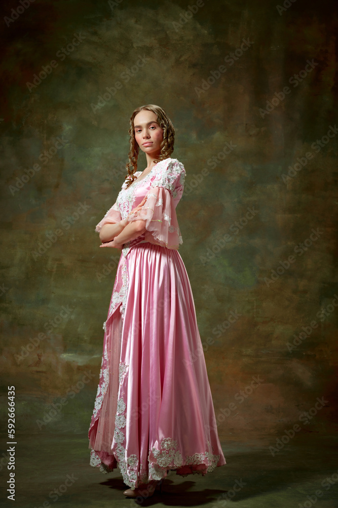 Portrait of charming blond girl, princess wearing fancy pink dress and standing with folded hands over vintage texture background. Serious lady