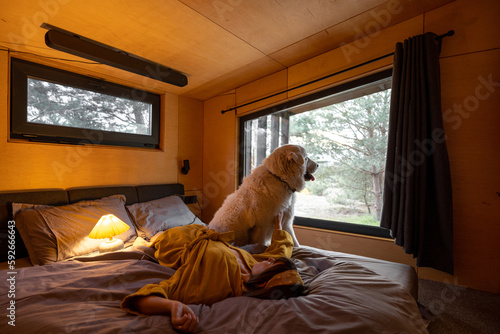 Woman lying with her huge adorable white dog in tiny bedroom while resting in wooden cabin on nature © rh2010