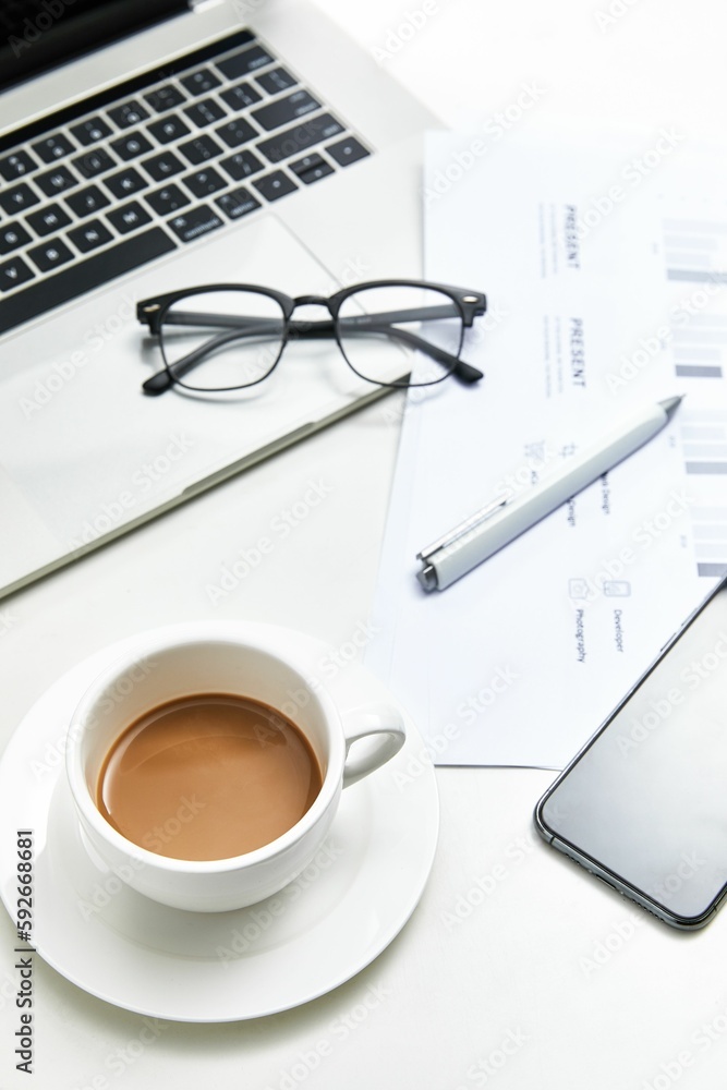 Vertical top view of a white office table with a notebook, glasses and a cup of coffee Vertical top view of a white office table with a notebook, glasses and a cup of coffee