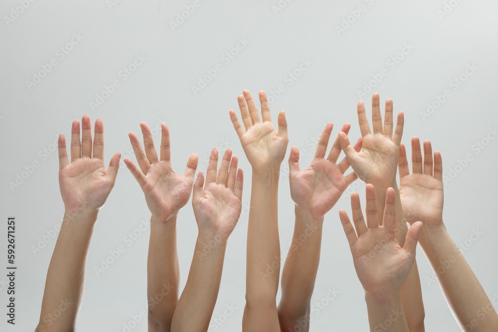 Many raised hands in a row on a grey background.