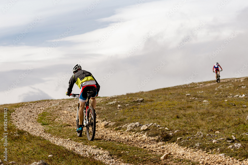 back male cyclist riding mountain bike on mountain gravel road in cross-country cycling race