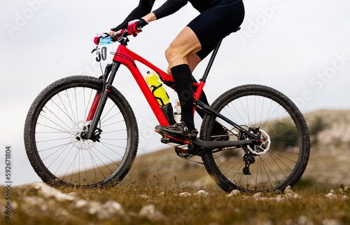 close-up male cyclist in compression socks riding on red mountain bike in cross-country cycling race