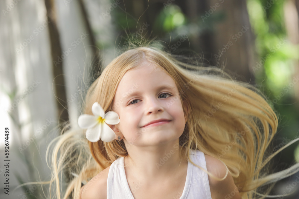 Candid outdoor portrait of adorable 5 years old girl with beautiful long blonde hair and frangipani flower behind ear, tropical vacation concept Candid outdoor portrait of adorable 5 years old girl with beautiful long blonde hair and frangipani flower behind ear, tropical vacation concept