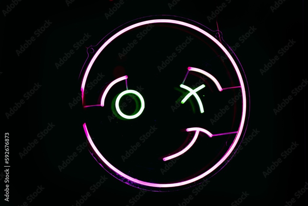 Neon sign of a winking emoji in Madrid Spain isolated on an empty black background Neon sign of a winking emoji in Madrid Spain isolated on an empty black background
