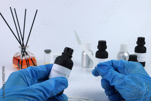 essential oil bottle is in left hand and blotting paper is in right hand  with background of fragrance oil bottles are used to blend nice scent for making perfume and candle by perfumer in  laboratory photo