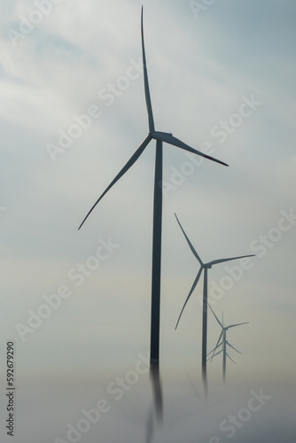 Windmills with rotor blades producing renewable green energy. Windmills turbines with rotor blades spinning on top for generating electricity in mist © SlavaStock