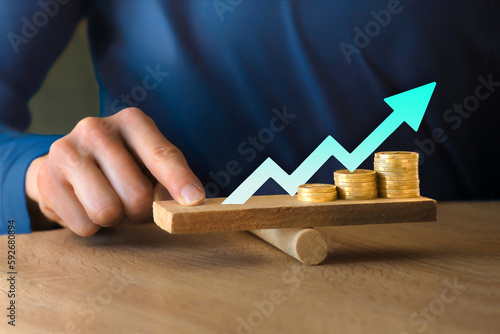 Money leverage and inflation balance. Business man Balancing Stacked Coins With Finger On Wooden Seesaw. Financial concept