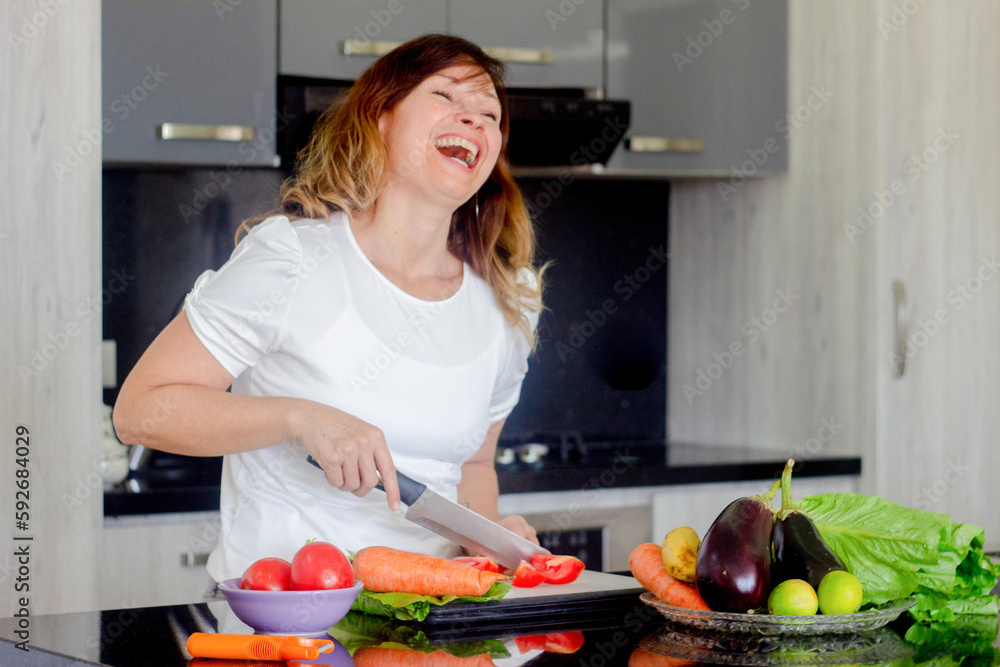 Beautiful young woman cooks food happy at the table in a modern kitchen on gray background