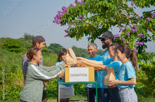 volunteers giving paper bag of food to asian senior woman and son,group of volunteers helping the needy to distribute of food items and water in the rural park photo