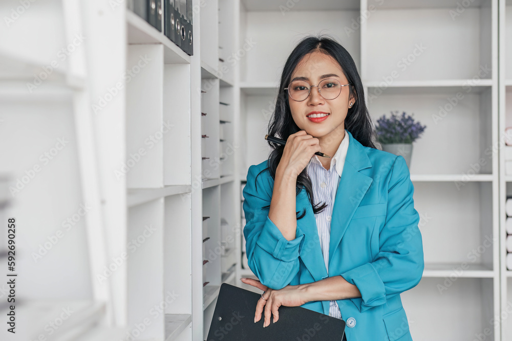 Smiling businesswoman holding stack of document and checking data on laptop computer standing at her desk office.