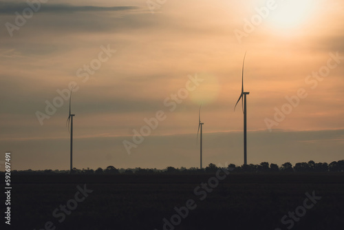 Sunset sun disk lights wind turbines with rotor blades on tops generating green energy as source of electricity. Windfarm at twilight
