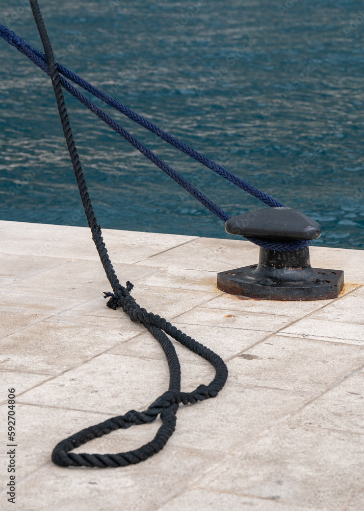 Light berth with mooring blue and black ropes tied around it leading to the ship. Against the backdrop of the blue sea