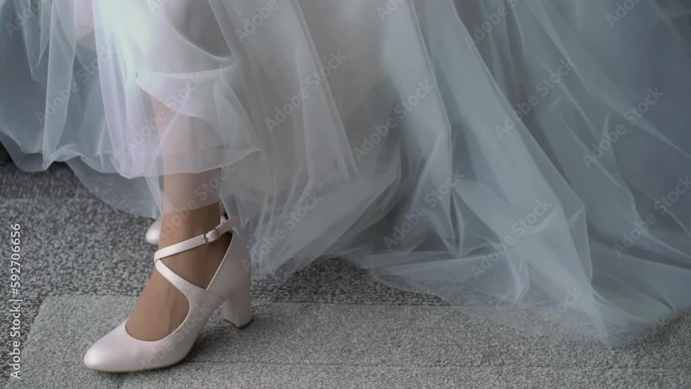 The bride in a white long luxurious wedding dress puts on high-heeled shoes. The bride in a white long luxurious wedding dress puts on high-heeled shoes.