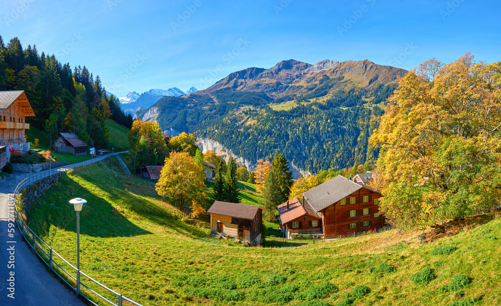Autumn panoramic mountain view with chalet on the meadow in the valley near Swiss alpine village Wengen.
