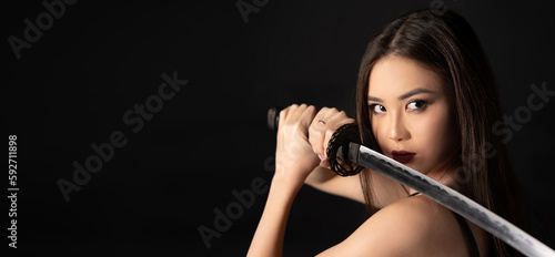 Portrait of pretty asian girl holding samurai katana sword on black background. Banner with copy space.