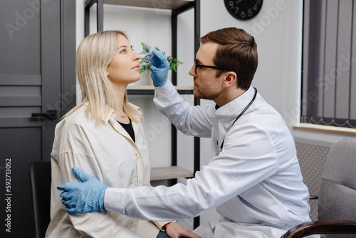 A young attractive otolaryngologist examining nose of a young patient during a medical examination in the ENT office photo