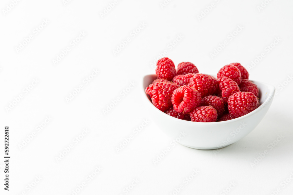 Overhead view of bowl with red raspberries on white background horizontal with copy space Overhead view of bowl with red raspberries on white background horizontal with copy space