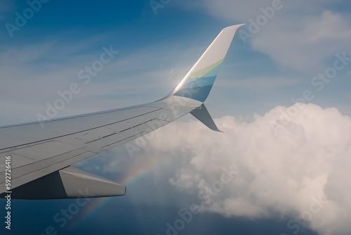 Wing view of the flying plane with a rainbow in the sky