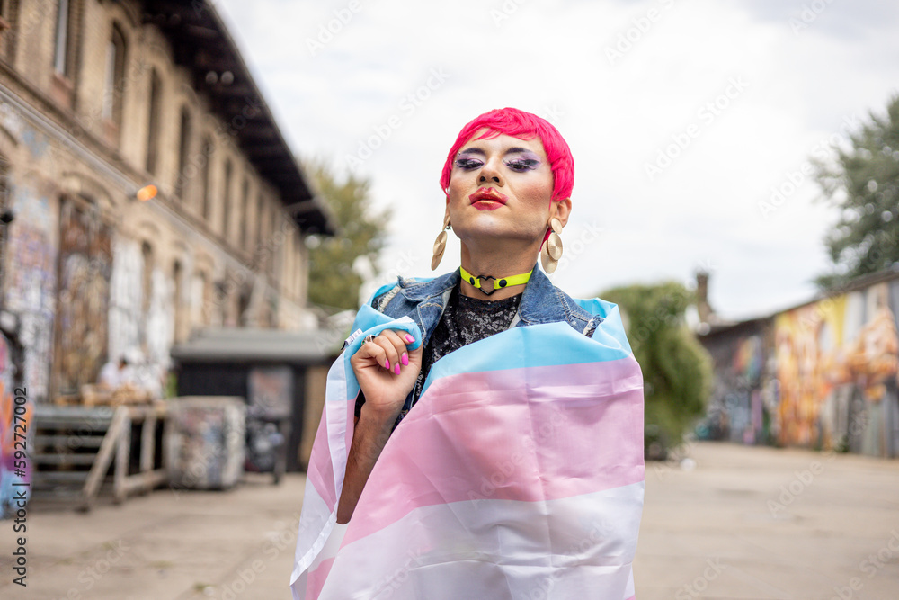 Queer person wrapped in a light blue and pink queer flag on the streets
