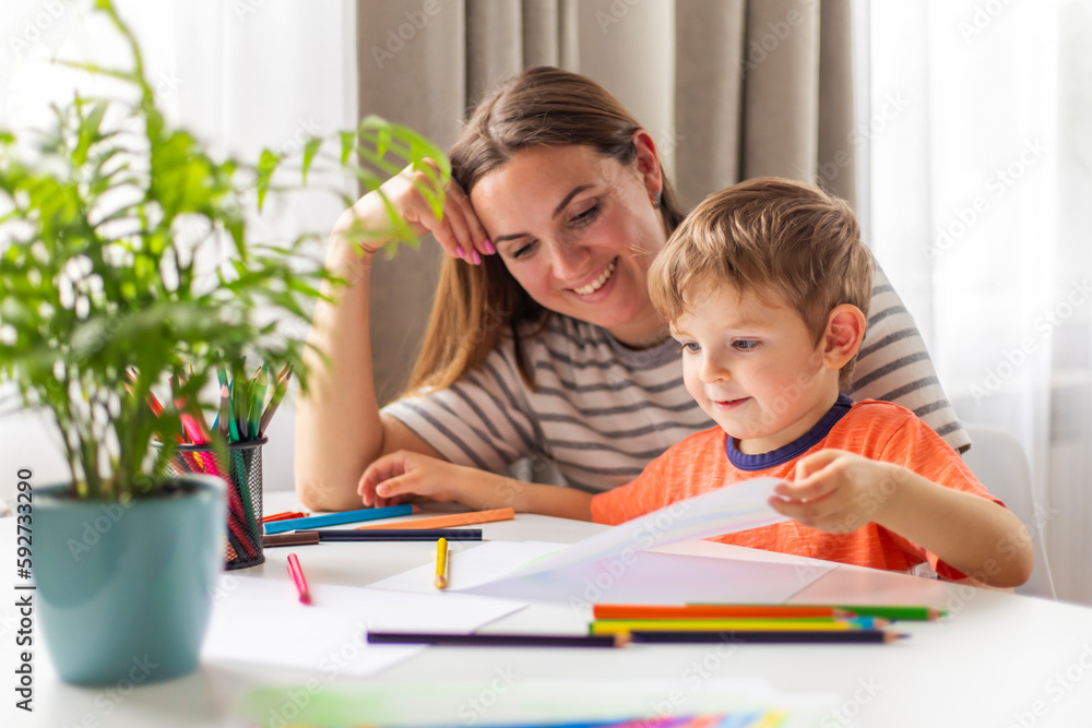 Mother and child drawing with pencils sitting at the desk at home